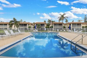 A swimming pool with lounge chairs and a fence, surrounded by buildings with balconies. - Harbour Lakes of Naples (Naples)