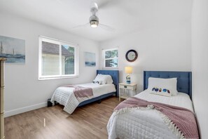 Ein Schlafzimmer mit zwei Betten, einem Deckenventilator, einem Nachttisch mit Lampe sowie Bildern an den Wänden.