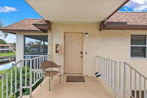 A covered porch with a door, a chair, a small rug, and a railing. - Harbour Lakes of Naples (Naples)