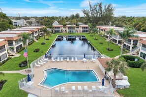 A swimming pool with lounge chairs and a flag, surrounded by buildings and greenery. - Harbour Lakes of Naples (Naples)