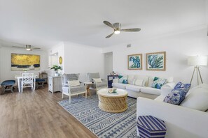 Ein Wohnzimmer mit Essbereich, weißen Möbeln, einem Deckenventilator und einem großen Gemälde an der Wand.