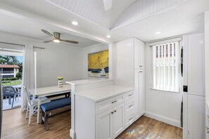 A modern kitchen with white cabinetry, a dining area with a bench, and a ceiling fan. - Harbour Lakes of Naples (Naples)