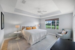 A bedroom with a bed, bedside tables, a chair, a window with a view, and a ceiling fan. - Heatherwood at Stonebridge - Golf (Naples)