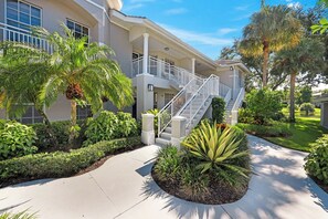 A multi-story building with a central staircase, surrounded by well-maintained landscaping and palm trees. - Heatherwood at Stonebridge - Golf (Naples)