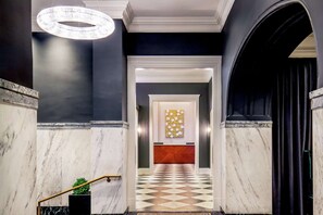 A hotel lobby with a marble floor, a chandelier, and a reception desk with a patterned backdrop. - Near James River + Rooftop Restaurant & Gym (Lynchburg)