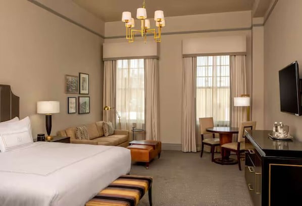 A hotel room with a large bed, a sofa, a desk, a chair, and a television. - Stay Near Riverwalk + Rooftop Restaurant (Lynchburg)