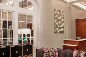 A lobby with a reception desk, a seating area with a sofa, and a decorative wall with a floral pattern. - 1BR King Steps to James River + Dining (Lynchburg)