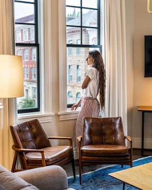 Una habitación con un ventanal grande, dos sillones de cuero, un sofá, una lámpara y un televisor de pantalla plana.