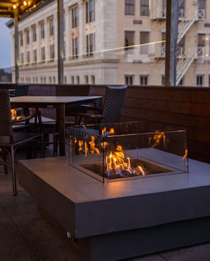 An outdoor seating area with a fire feature, tables, and chairs. - Stay Lynchburg Iconic Building + Rooftop Dining (Lynchburg)