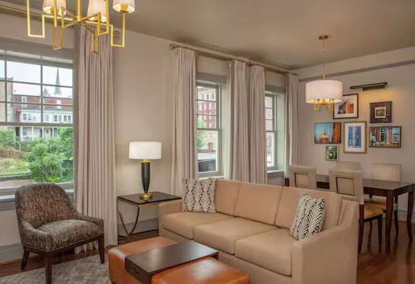 A modern living room with a sofa, armchair, and a dining table. - Stay Lynchburg Iconic Building + Rooftop Dining (Lynchburg)