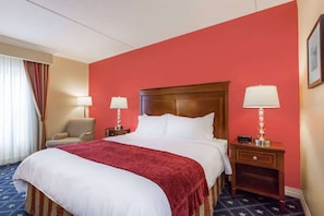 Habitació d'hotel amb un llit gran, dues taules de nit, una cadira i una finestra amb cortines.