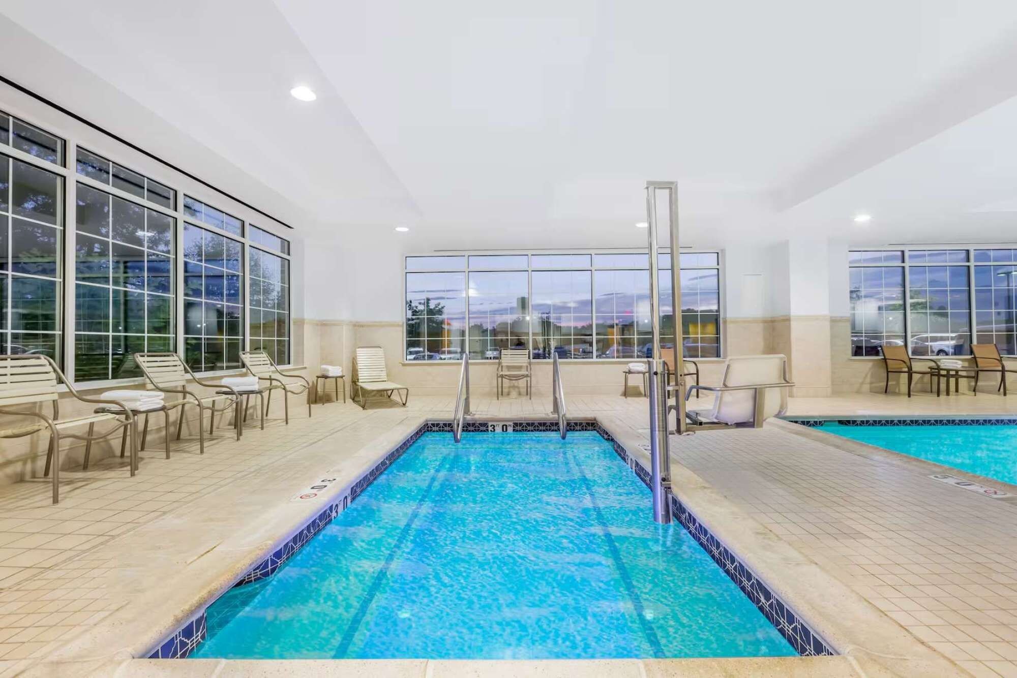 Une piscine intérieure à l’eau d’un bleu cristallin, entourée de chaises longues et offrant une vue sur l’extérieur.