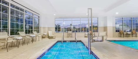 An indoor swimming pool with clear blue water, surrounded by lounge chairs and a view of the outside.