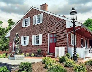 Une maison en briques rouges, avec une clôture en bois peinte en blanc, une statue et un lampadaire.