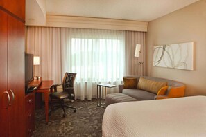 Een hotelkamer met een bed, een bureau, een stoel, een klein tafeltje en een raam met gordijnen.