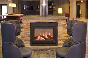 Une cheminée en pierre avec un feu, flanquée de deux fauteuils à motifs étoilés, dans une pièce équipée d’une télévision et dotée d’étagères au-dessus.