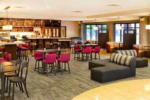 Een hotel lobby met een bar, verschillende zitplaatsen, waaronder tafels en stoelen, en een bank.