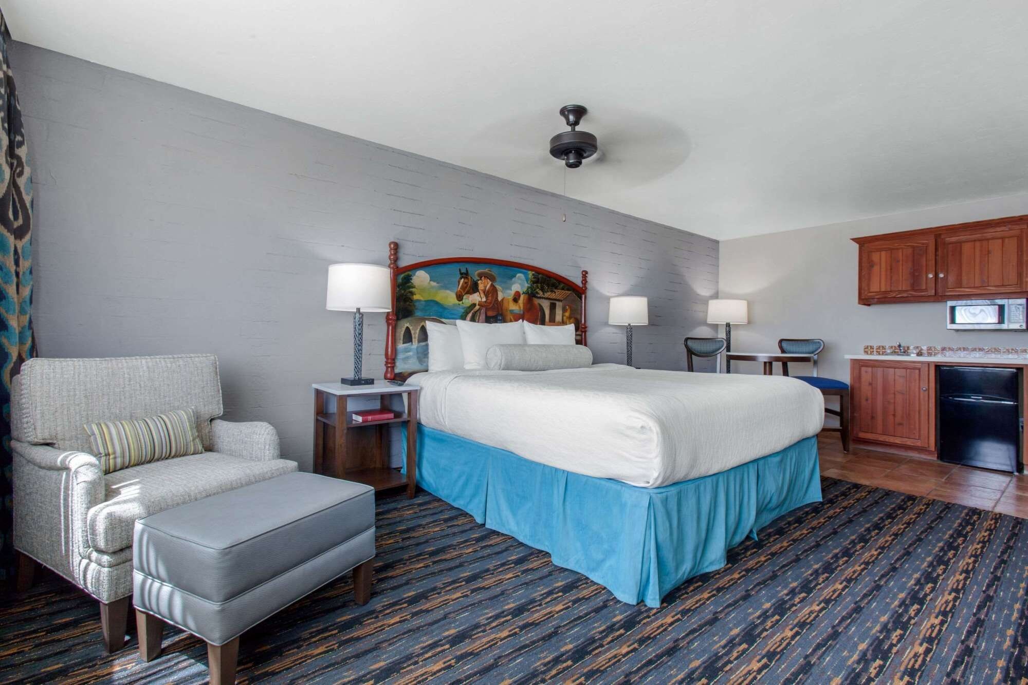 A hotel room with a bed, a chair, a desk, a microwave, and a cabinet.