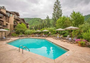 A swimming pool with lounge chairs and umbrellas, surrounded by lush greenery and a mountainous backdrop. - 1BR  w/Kitchen + 2 Heated Pools & Town Shuttle (Vail)