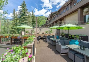 An outdoor patio with wicker furniture, green umbrellas, and potted plants. - 3BR w/Kitchen & Balcony + 2 Heated Pools & Town Shuttle (Vail)