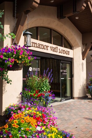 The entrance to Manor Vail Lodge with a large arched doorway, a hanging lantern, and vibrant flower arrangements. - 3BR w/Kitchen & Balcony + 2 Heated Pools & Town Shuttle (Vail)