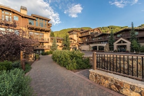 A multi-story building with a stone facade, a paved walkway, and a mountain backdrop. - 2BR Penthouse w/Kitchen & Balcony + 2 Heated Pools (Vail)