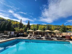 Una piscina amb gandules i ombrelles, envoltada d'arbres i un paisatge de muntanyes.