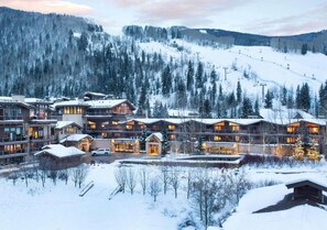 Un rifugio imbiancato dalla neve con diversi edifici, una seggiovia sullo sfondo e un paesaggio montuoso.