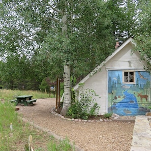 A rustic cabin with a colorful mural on the door, surrounded by a gravel path and a picnic table. - 4BR Penthouse w/Kitchen & Loft + 2 Heated Pools (Vail)