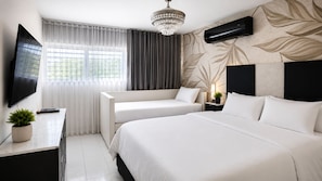 Habitación de hotel con cama, sofá, televisión, planta y ventana con cortinas.