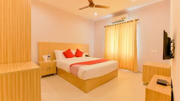 A hotel room with a bed, bedside tables, a desk, a ceiling fan, and a TV mounted on the wall.