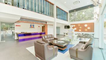 A spacious lobby with a reception desk, leather sofas, a glass coffee table, and a decorative wall with lights.