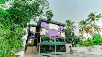 Um edifício moderno de vários andares com telhado plano, cercado por vegetação exuberante e palmeiras.