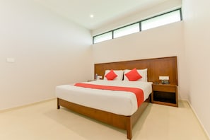 A hotel room with a large bed, a wooden headboard, a nightstand with a phone, and a window above the bed. - Super Townhouse Edassery Blue Bells (Kochi)