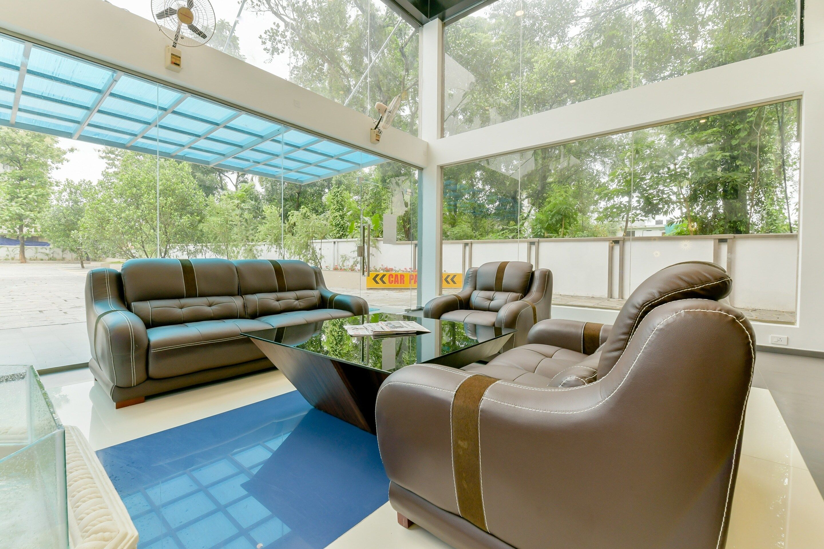 Uma área de estar moderna em ambientes internos, com sofás e poltronas de couro, uma mesa de centro de vidro e grandes janelas com vista para o exterior.