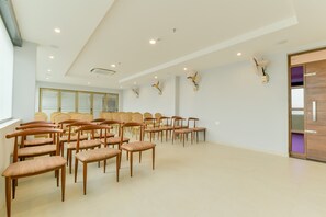 A conference room with rows of wooden chairs, ceiling fans, and recessed lighting. - Super Townhouse Edassery Blue Bells (Aluva)