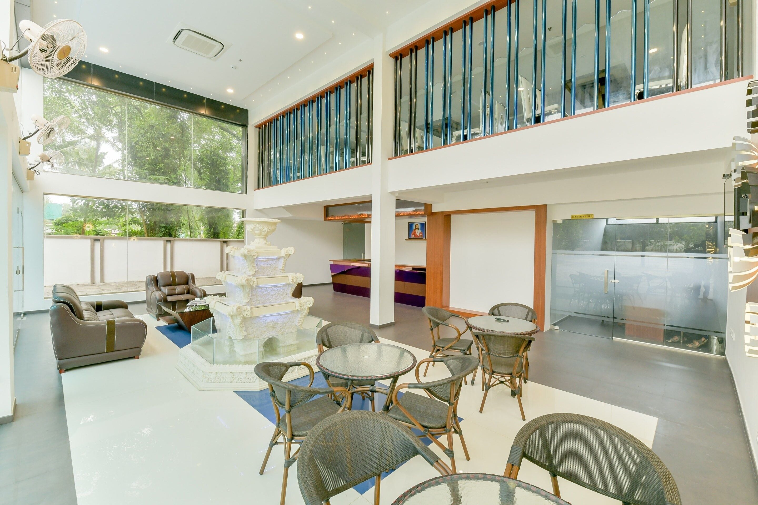 Un amplio espacio interior con zona de estar que incluye sofás y sillas, una fuente decorativa blanca y una mesa de vidrio.
