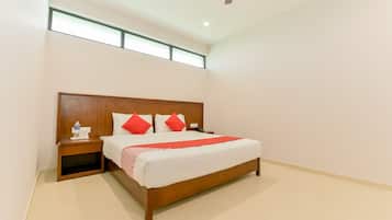 A hotel room with a large bed, wooden headboard, a nightstand, a water bottle, and a red throw blanket.