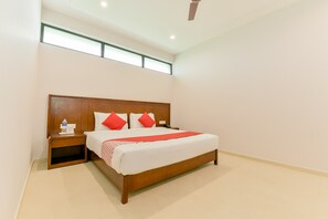 A hotel room with a large bed, wooden headboard, a nightstand, a water bottle, and a red throw blanket. - Super Townhouse Edassery Blue Bells (Aluva)