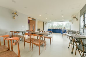 A spacious dining area with multiple tables and chairs, a large window providing natural light, and ceiling fans for ventilation. - Super Townhouse Edassery Blue Bells (Kochi)