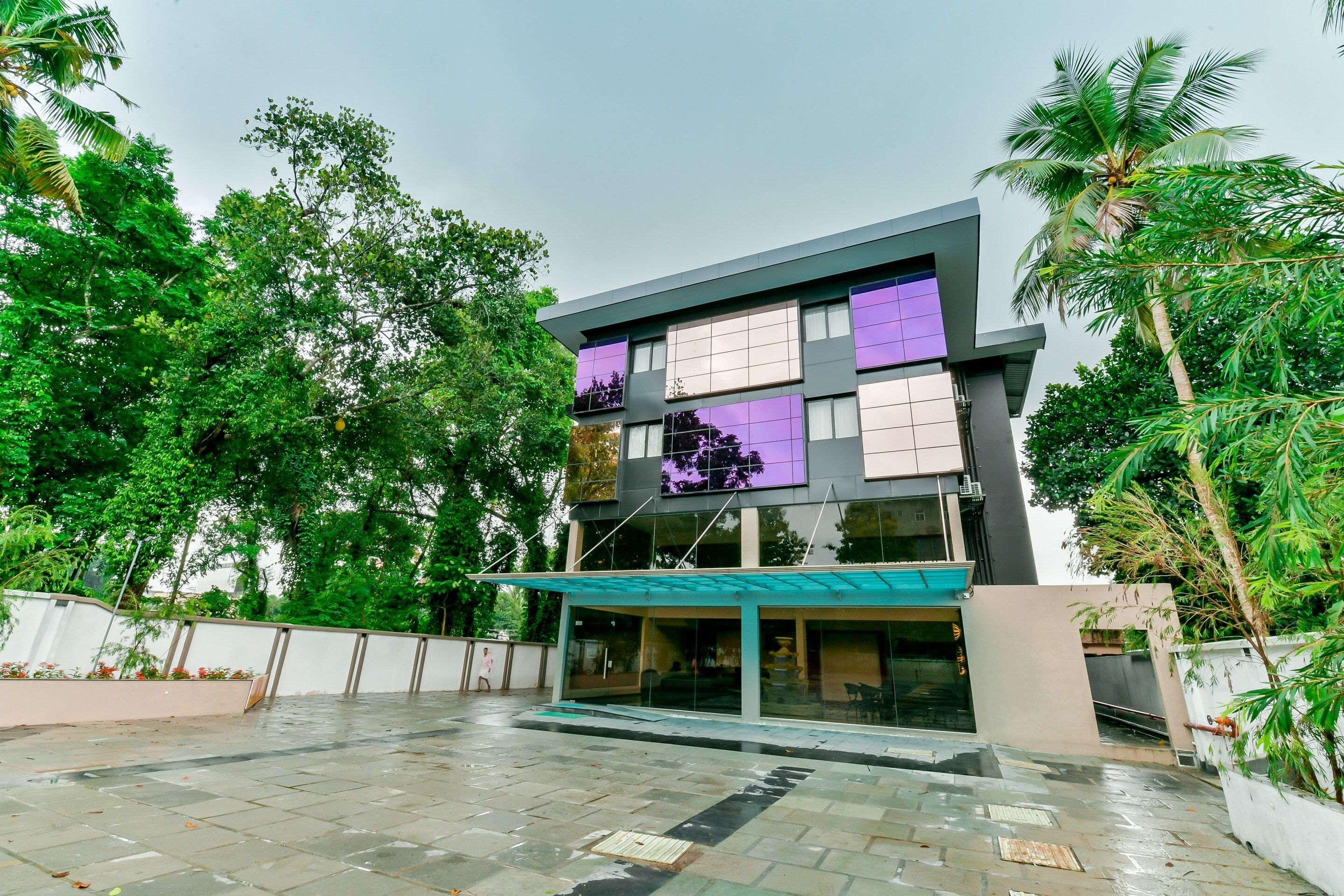 A modern building with a glass facade, surrounded by lush greenery.