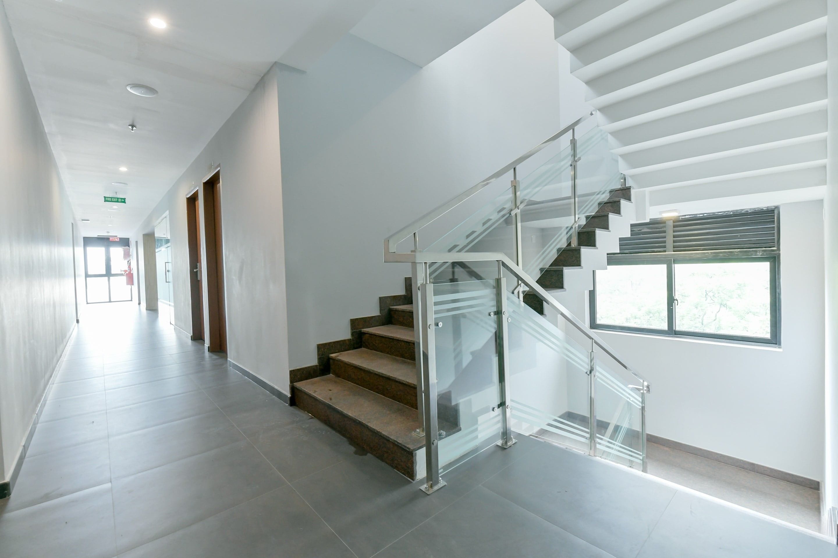 Een modern interieur met een glazen trap, een lange gang en een deur met de tekst 'Fire Exit'.