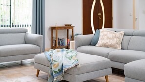A modern living room with a grey sofa, a matching ottoman, and a small wooden side table with books. - Wongaling Whispers~ Escape to the gentle rhythm of Wongaling Beach (Wongaling Beach)