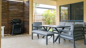An outdoor patio with a grill, seating, and a view of the backyard. - Wongaling Whispers~ Escape to the gentle rhythm of Wongaling Beach (Wongaling Beach)