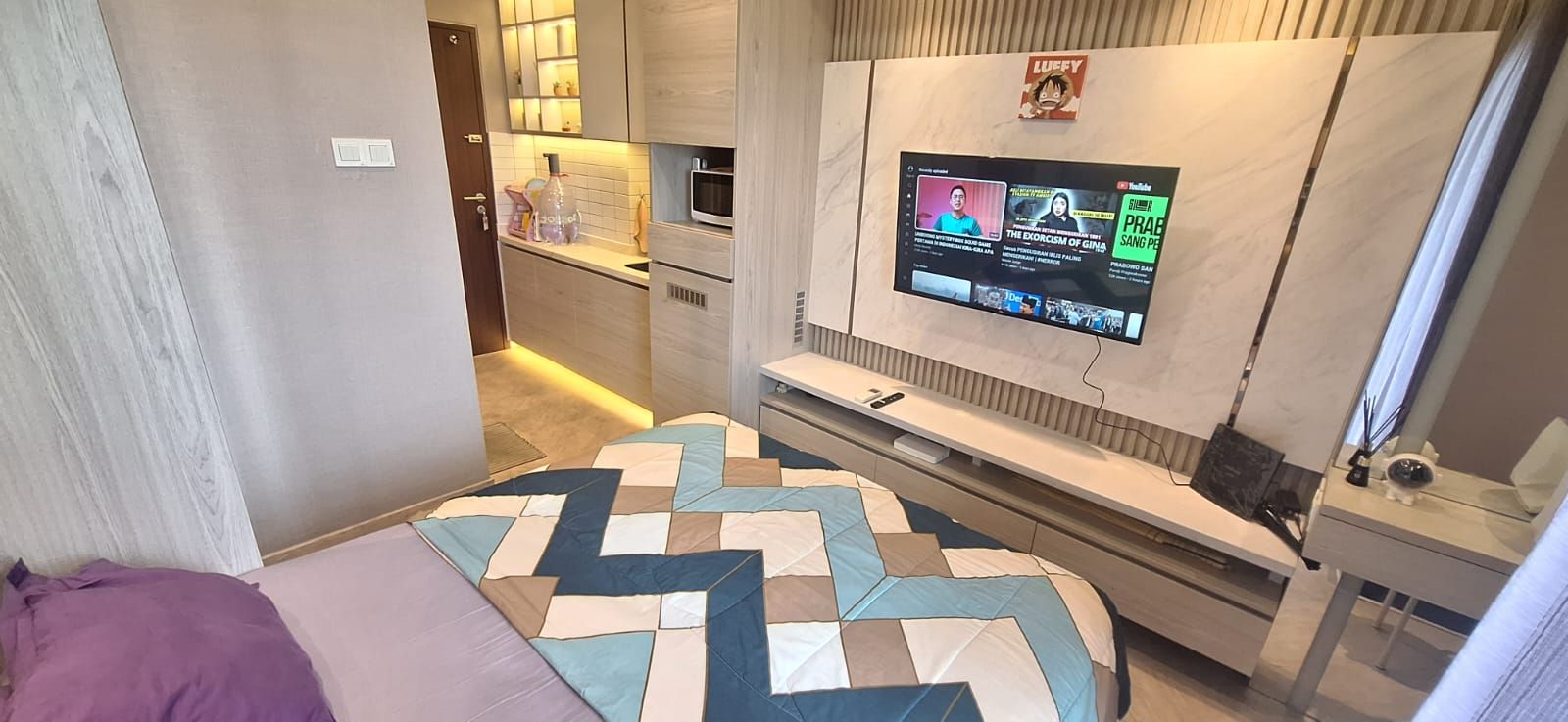 A compact bedroom with a bed, a TV mounted on the wall, and a small bedside table.