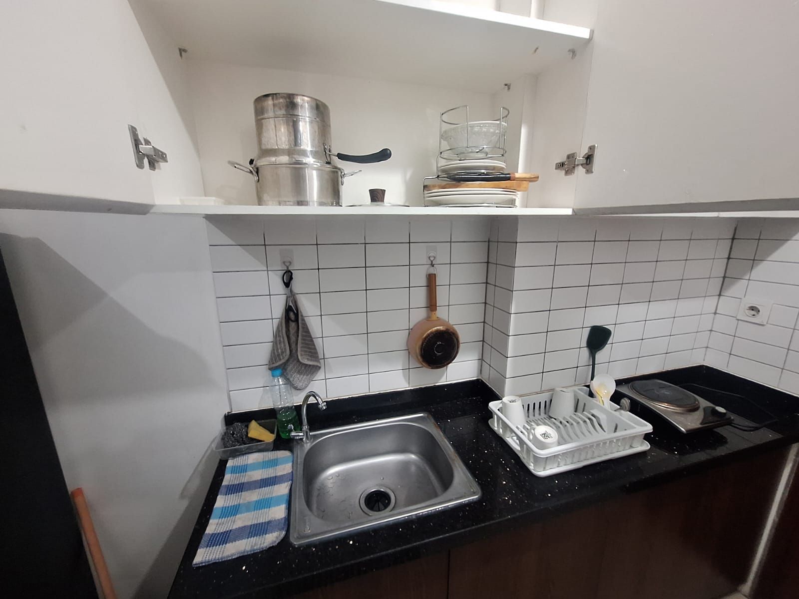 Una cocina con un lavamanos de acero inoxidable, un escurreplatos, una tetera y un colgador para ollas.