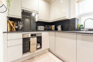 A modern kitchen with white cabinetry, a built-in oven, a microwave, and a coffee maker. - Peaceful Returns - 2 Bed House Near Roundhay Park (Leeds)