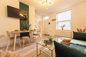A modern living room with a flat-screen TV, a dining area with a table and chairs, a sofa, and a coffee table. - Peaceful Returns - 2 Bed House Near Roundhay Park (Leeds)