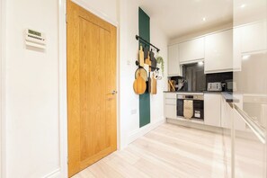 Een moderne keuken met witte kasten, een houten deur en een groene accentmuur.
