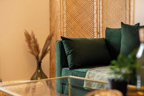 A green sofa with a cushion, a glass coffee table, and a vase with dried plants. - Peaceful Returns - 2 Bed House Near Roundhay Park (Leeds)